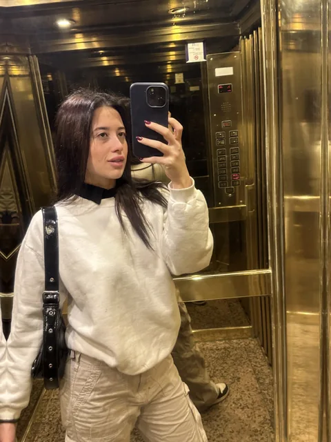 Natalye taking a mirror photo in a cream sweater and trousers