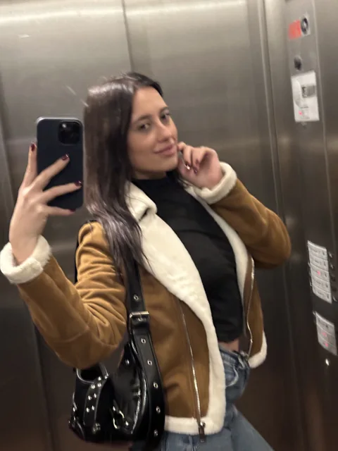 Natalye taking a mirror photo in a brown jacket